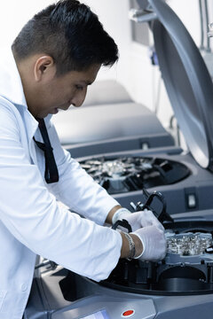 Young, Latino, professional-looking laboratory and blood bank technician wearing a white coat and gloves, carrying out processing of whole blood for the benefit of patients who require it.