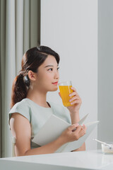 Asian woman reading a book and hold orange juice glass in the home - 653085771