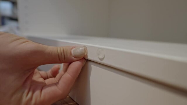 Close-up of hands sticking protective rubber bumper on white closet