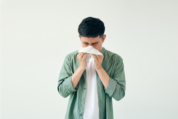 Young man wiping his nose with a tissue on white background