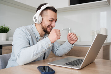 Young man with laptop and headphones indoors at home, studying, freelance working