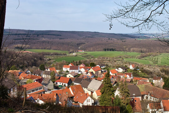 Sun shining on houses with red roofs in a small German village on a sunny spring day with fields and hills in the distance.