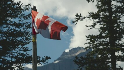 The canadian flag against the sky on a blue sunny day, in the rocky mountains of Canada at Moraine Lake in Banff National Park, Alberta 