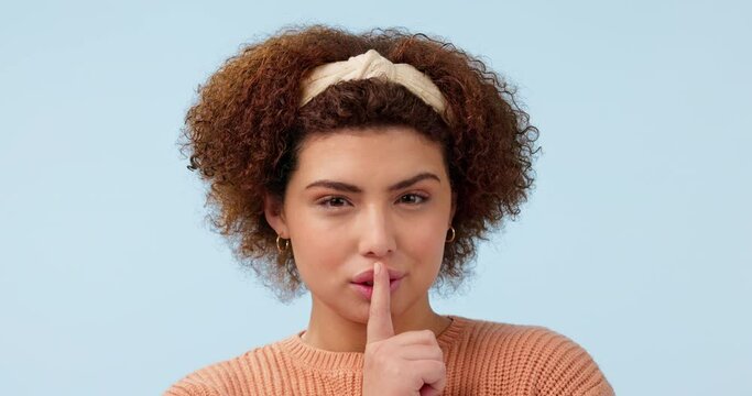 Whisper, face and woman with finger on lips in studio for secret, news or hush on blue background. Gossip, portrait and lady model with privacy, confidential or emoji for drama, announcement or mute