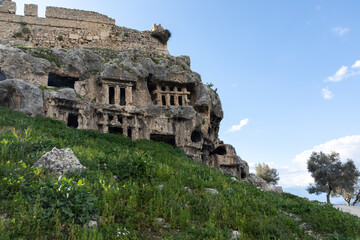 Gray rock-cut ancient ruins and ruined dead city: carved windows, passages, doors, arches. Remains of ancient Lycia civilization, Tlos antique city in Turkey.  Mountain landscape in the background.