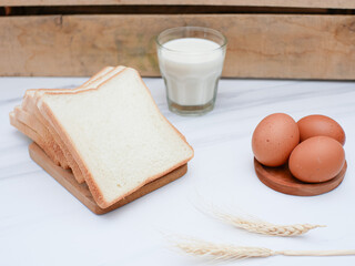 sliced white bread on the wooden cutting board. with a glass of milk and an egg