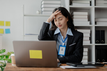 A woman sits in a company office and looks stressed. A businesswoman is stressed and tired from working hard. She works for a long time causing office syndrome. The concept of stress from work. - obrazy, fototapety, plakaty