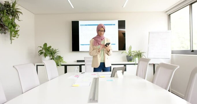Biracial casual businesswoman in hijab talking on smartphone in meeting room, slow motion