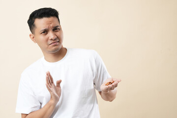 A young Asian man standing with an outstretched hand showing a stop sign, refusing to eat almonds.