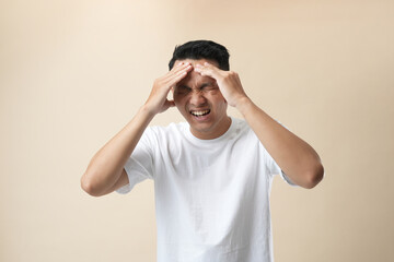 Fototapeta na wymiar Young Asian man isolated on beige background, suffering from headache, desperate because of pain and migraine. Hands on head.