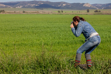 Naklejka na ściany i meble A woman taking pictures in a vast prairie landscape amidst a field of lush green grass. With copyspace to add text or graphics.