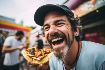 Rolgordijnen Young man eating a taco on a street food festival. Street food concept. © Nerea