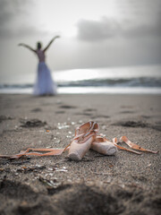 Pointe shoes on the sand , a ballerina in the background.