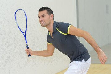 man poised holing raquet on squash court