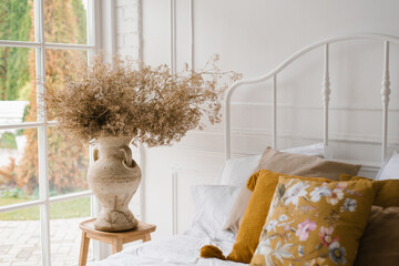 Dried flowers in a classic vase on the bedside table with pillows near the French window