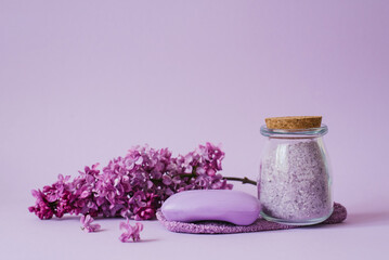Obraz na płótnie Canvas Cosmetic spa set for body care. Sea salt in glass jar, organic soap, washcloth glove and lilac flowers on purple background