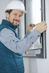 young engineer using tape measure for measuring window at site