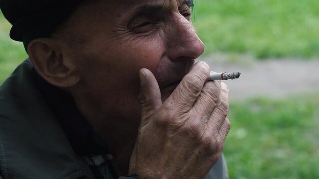 portrait of a Caucasian pensive pensioner, 70 years old, smoking a filter cigarette while outside in autumn clothes and shitty attire. A pensioner of European appearance smokes