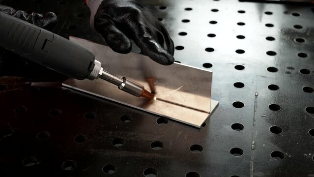 Laser welding machine with a hand gun. Laser welding of two aluminum parts is shown in close-up.