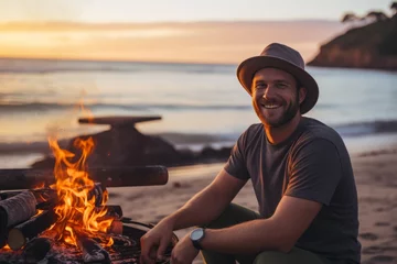 Gordijnen Young man sitting by the fire on the beach at sunset. Camping concept. © Nerea