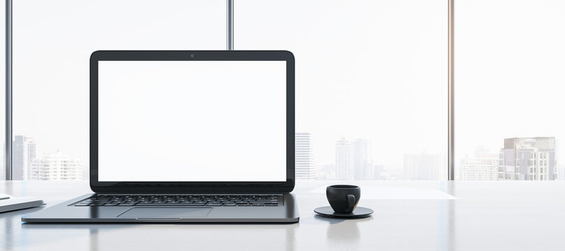 Close up of clean workplace with empty white mock up laptop screen, supplies, coffee cup and panoramic window with city view in the background. 3D Rendering.