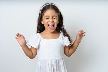 Emotive beautiful kid girl wearing white dress laughs loudly, hears funny joke or story, raises...