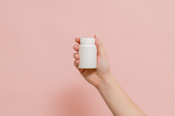 Plastic bottle (tube) in hand on pink background. Packaging for vitamins, tablets or capsule, or supplement