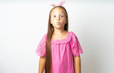 Shot of pleasant looking beautiful kid girl wearing pink dress , pouts lips, looks at camera, Human...