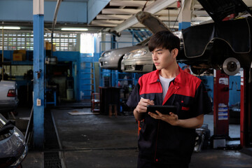Fototapeta premium One male Asian professional mechanic, supervisor engineer, inspects repair work checklists with tablet at garage, service car maintenance, and fixing specialist occupations in auto transport industry.