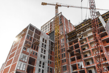 Bottom view of an unfinished multi-story residential building under construction with a working construction crane against a clear blue sky