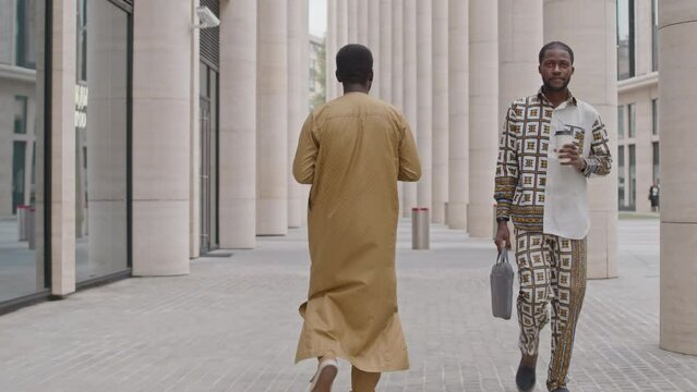 Slowmo full length shot of two young handsome Black men in stylish outfits walking down street in city downtown