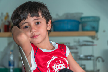 A boy wear red shirt sitting in the kitchen during waiting for a meal