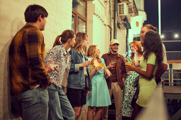 Stylish young people, friends meeting in evening outdoors, on rooftop, drinking, talking, having fun together. Concept of party, leisure time, fun and joy, weekends, celebration, youth culture
