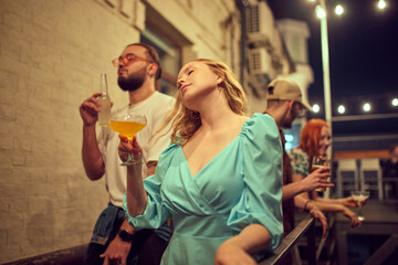 Young cheerful people, men and women meeting in evening outdoor, having good time, dancing and drinking. Concept of party, leisure time, fun and joy, weekends, celebration, youth culture