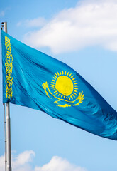 The flag of Kazakhstan is fluttering in the wind against the blue sky. The flag is located on the blue dome of the administrative building. The city of Astana is the administrative center.