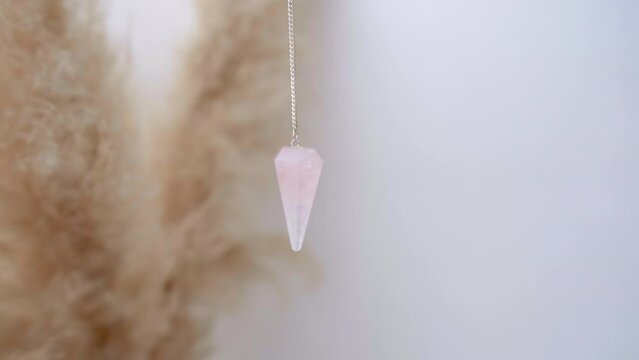 Rose quartz crystal pendulum hanging from a chain swinging in an esoteric divination and holistic mystical ritual
