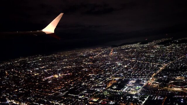 View of the airplane wing from the window during a night flight taking off or landing, city aerial landscape and the lights of the City glow and shining in the background