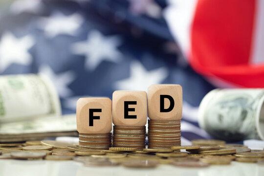 The Federal Reserve ( FED ) to control interest rates. Wooden blocks FED on coins with USA flag background. American economy and business. Federal Reserve Bank Interest rates rise policy. FED concept.