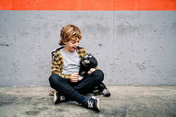 Happy kid sitting near concrete wall and looking at dog