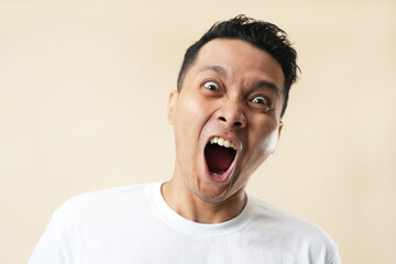 Portrait of an aggressive Asian man, isolated on beige background.