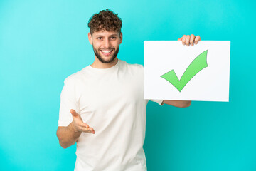 Young handsome caucasian man isolated on blue background holding a placard with text Green check...