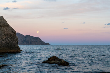 Sudak, Crimea. Moon rise. Cape Rybachy. Mount Meganom in the light of the setting sun