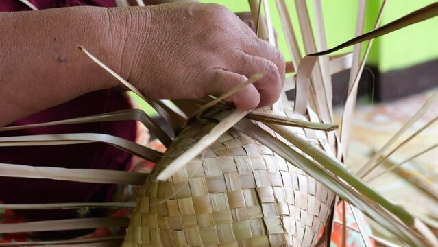 An Indonesian woman´s hand weaving an ancestral basket case from mangrove palm leaves . People is demonstrating weaving basket made from nipa palm. Weaving a traditional basket made from mangrove palm
