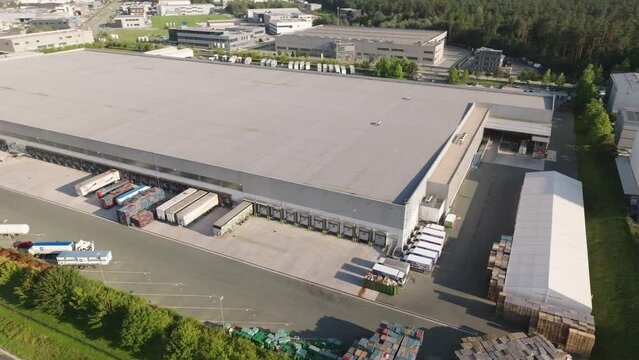 Logistics and distribution warehouse building with trucks at parking aerial view. Flying around shipment storehouse and lorry trailers drone shot