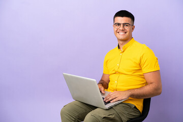 Young man sitting on a chair with laptop laughing
