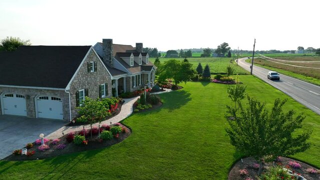 American home with beautiful landscaping in summer. Flowers blooming in lawn at sunset. Aerial establishing shot of farm house in rural USA.