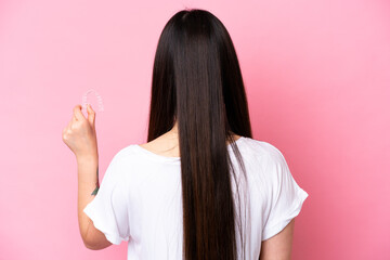 Young Chinese woman holding invisible braces isolated on pink background in back position - obrazy, fototapety, plakaty