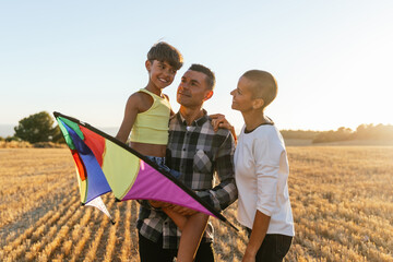 Mom, dad and daughter together holding a colorful kite on a sunny day. - obrazy, fototapety, plakaty