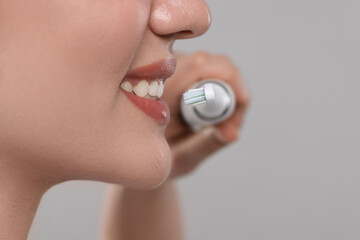Fototapeta premium Woman brushing her teeth with electric toothbrush on light grey background, closeup. Space for text