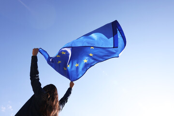 Woman holding European Union flag against blue sky outdoors, low angle view - obrazy, fototapety, plakaty